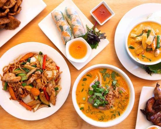 Non La dishes on a table: stir-fried noodles, rice paper rolls with dipping sauce, laksa and a curry